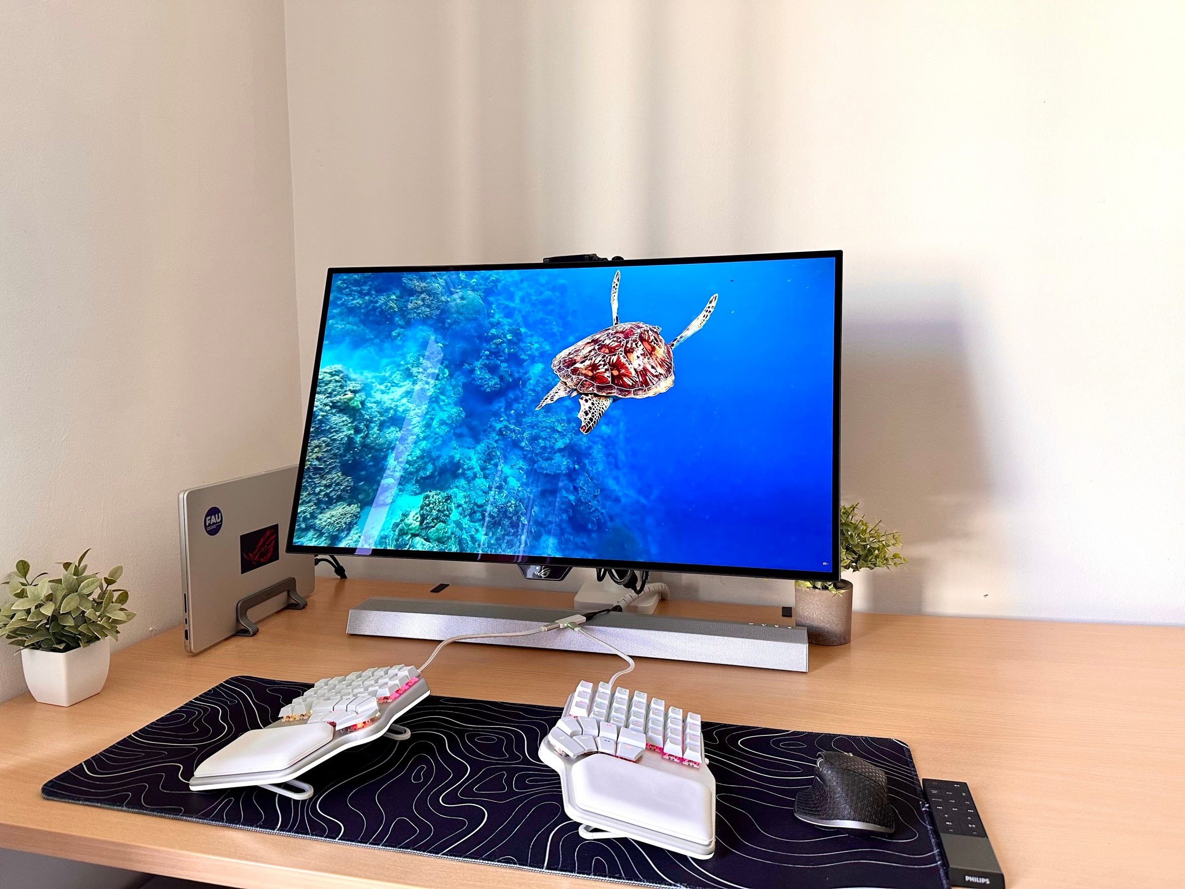 Desk with an external monitor, a closed MacBook Pro in a vertical stand and the split keyboard on a desk mat