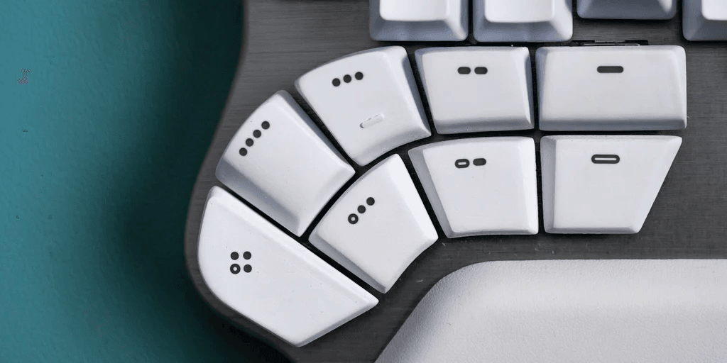 Close-up of one half of a Dygma Defy. Eight white thumb keys are arranged in two curved rows, with a gray palm rest below and the edge of the main key block above.