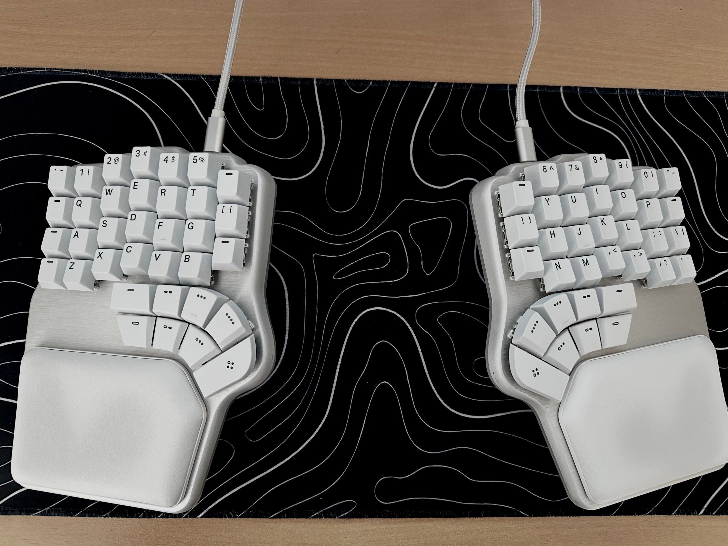 White Dygma Defy split keyboard on a black desk mat with a topographic pattern